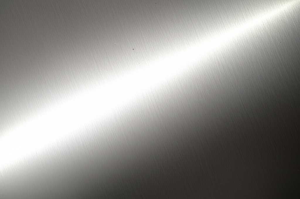 Close-up conceptual image highlighting the interplay of light on a metal print that shows both a glossy section and a textured section. Abstract and artistic, not showing a full product.