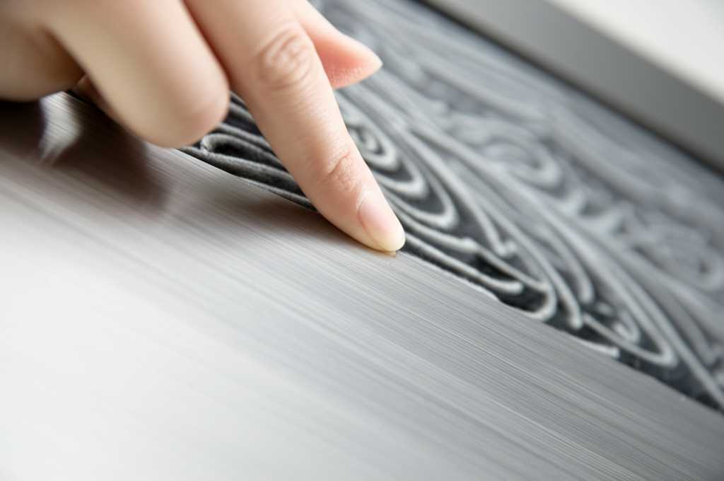 Close up of a hand gently touching textured metal art