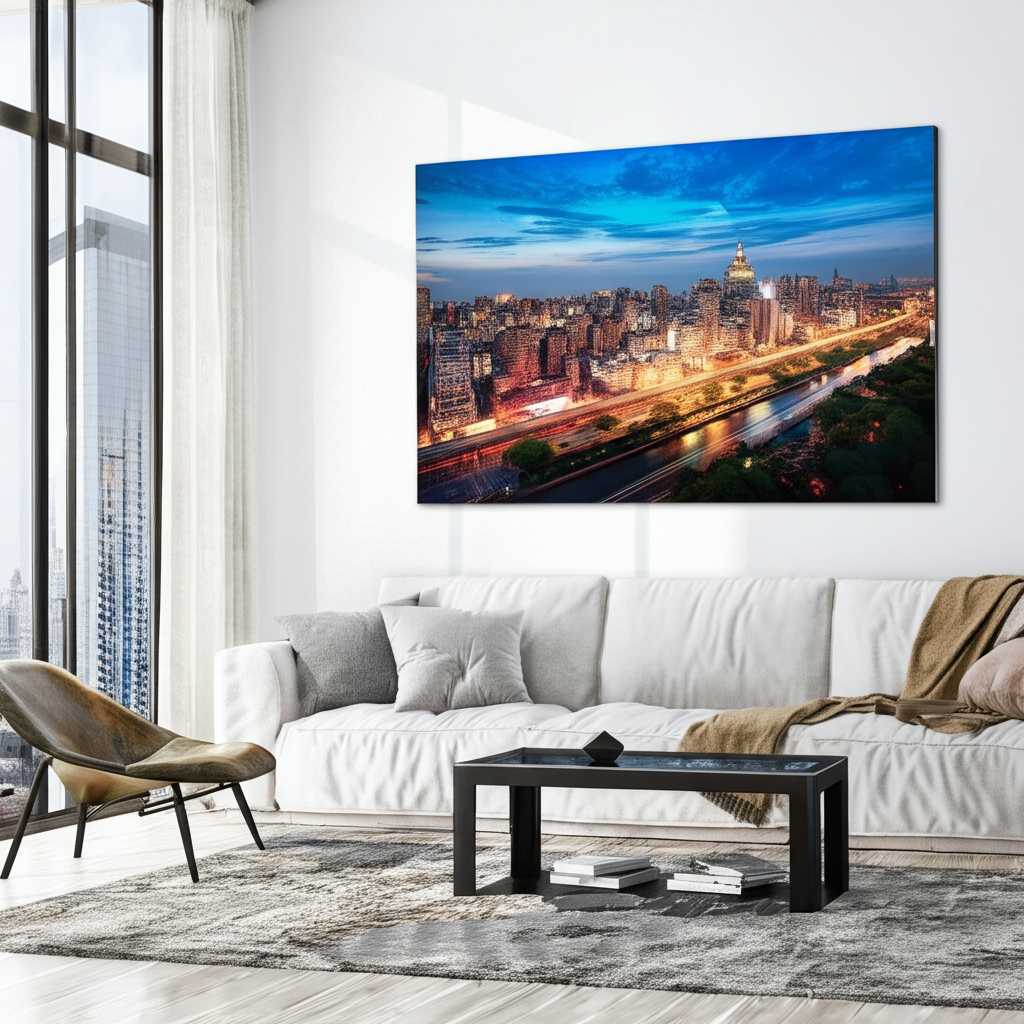 A large, horizontal metal print depicting a panoramic cityscape dramatically hung above a long, low-profile sofa in a modern living room with ample natural light.