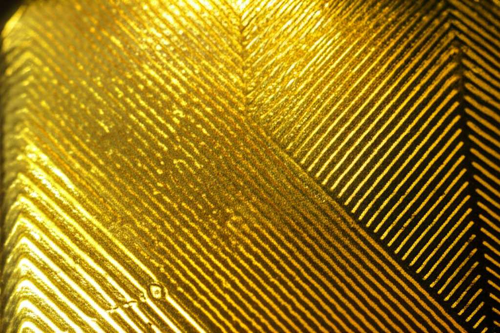Abstract macro shot of intricate, raised texture on a metallic surface with rich, luminous colors and light play