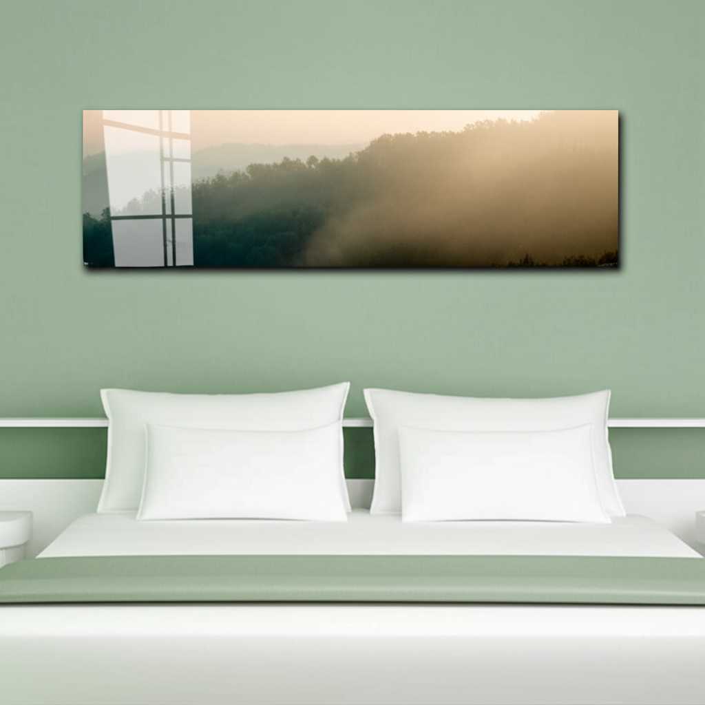 A serene and minimalist bedroom with a neutral color palette. Above the upholstered headboard hangs a horizontal panoramic metal print of a tranquil, misty mountain range, adding a sense of calm and depth to the space.