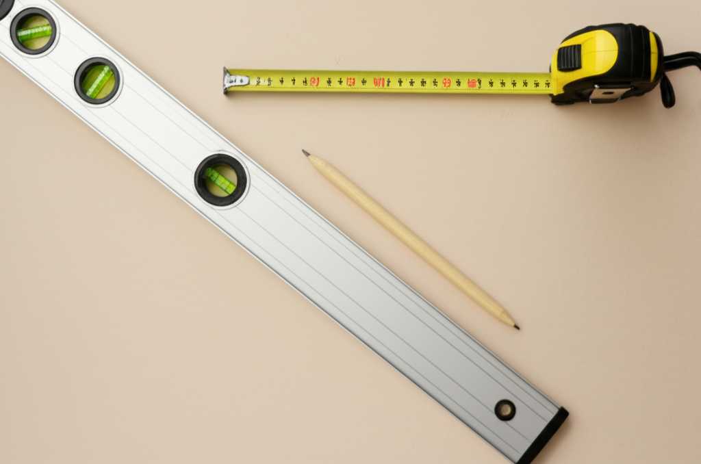 A stylish flat lay of essential art hanging tools – level, measuring tape, pencil – thoughtfully arranged beside a conceptual, generic metal print ready for mounting.