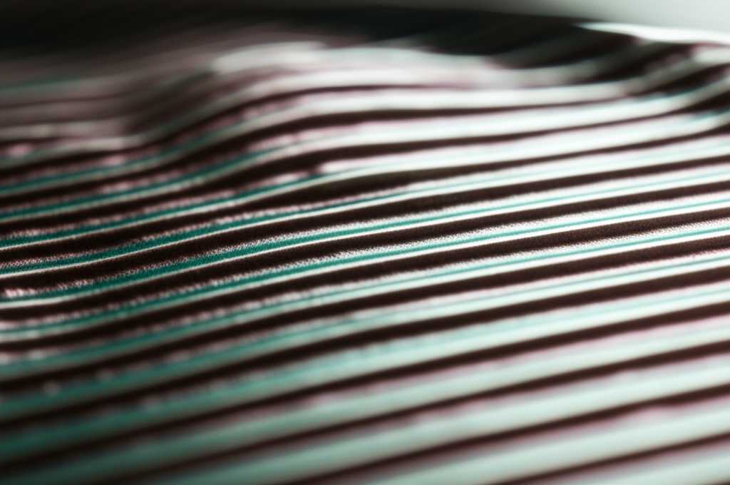 An abstract close-up of a metal art piece, showing light playing across a textured, glossy surface, highlighting subtle ridges and a deep, liquid-like shine.