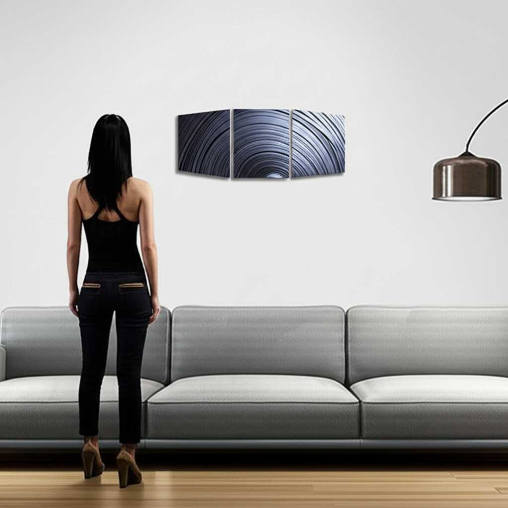 A person standing back and admiring a perfectly hung triptych of metal art above a minimalist sofa in a beautifully lit living room.