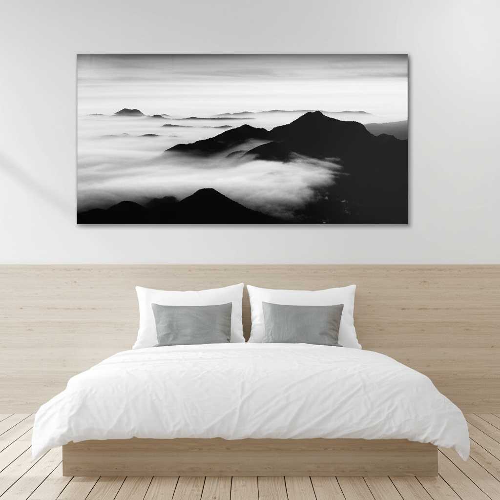 A serene, minimalist bedroom with a large, panoramic metal print of a tranquil, misty mountain range in monochrome hanging above a neatly made bed with white linens.