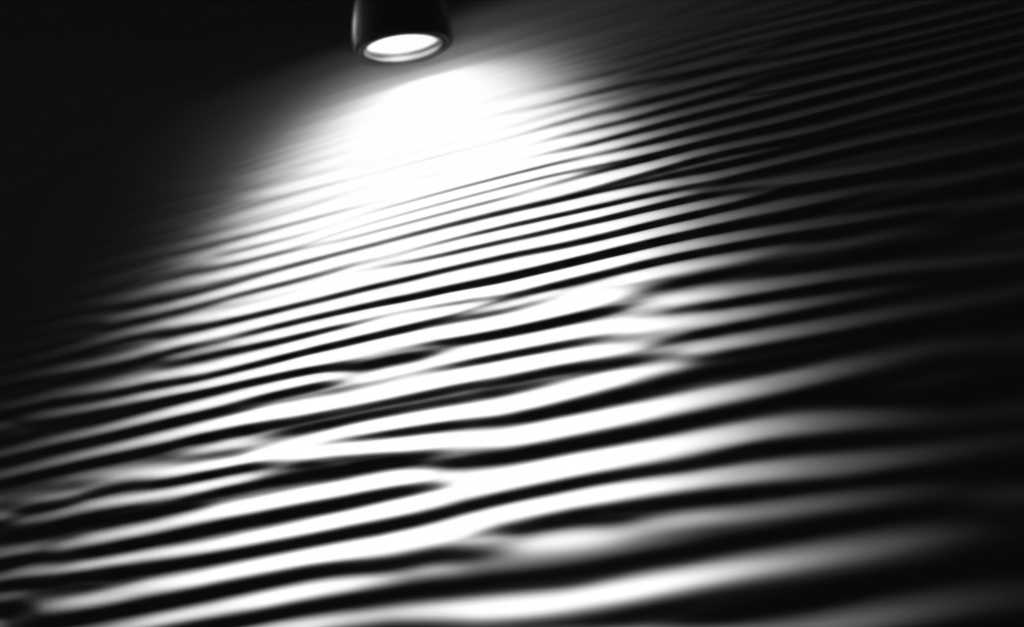 Close-up perspective of a textured metal art piece under a focused picture light, emphasizing its surface details and sheen.